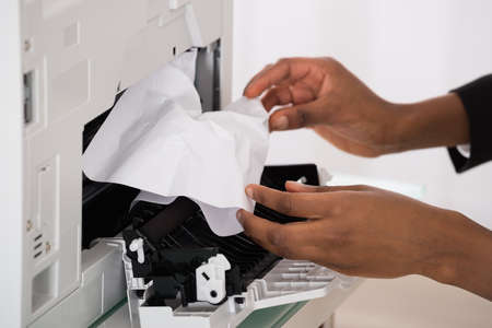 Close-up Of Businesswoman Hand Removing Paper Stucked In Printer At Officeの写真素材