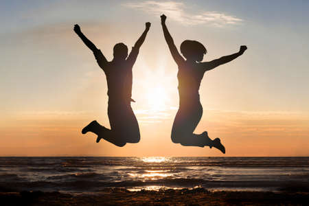 Silhouette Of Man And Woman Jumping At Beach During Sunset