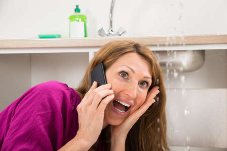 Close-up Of Woman Calling To Plumber While Water Leaking From Sinkの写真素材