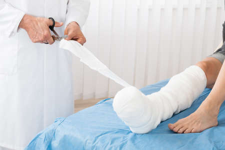 Close-up Of Doctor Bandaging Leg Of Patient Lying On Bed In Hospitalの写真素材