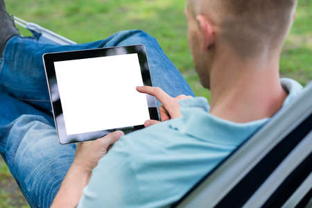 Young Man Using Digital Tablet While Lying In Hammock