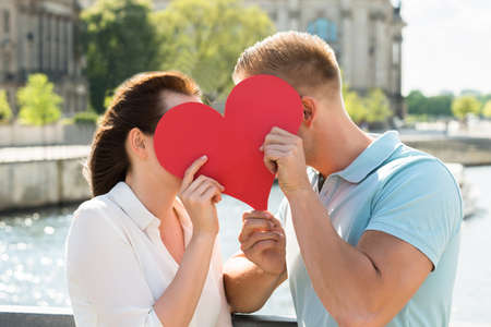 Close-up Of Young Couple Hiding Behind Heart Shapeの写真素材