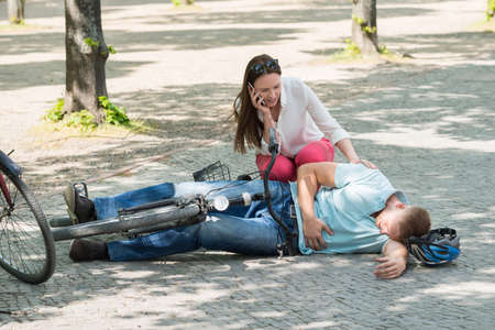 Worried Woman Calling For Help After Man Getting Injured By Falling From Bicycleの写真素材