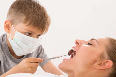Close-up Of Little Boy Examining Teeth Of Young Woman