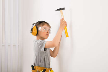 Cute Little Boy Hammering Nail In Wall At Homeの写真素材