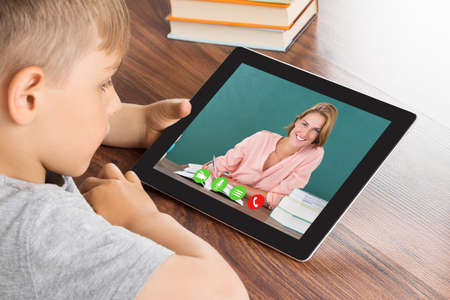 Close-up Of Cute Little Boy Videoconferencing On Digital Tablet In Classroom