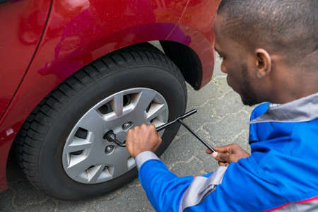 Young African Mechanic Changing Tire Of A Red Car With Wrenchの写真素材