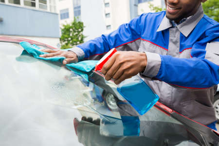 Young Male Worker Cleaning Car Windshield With Cloth And Spray
