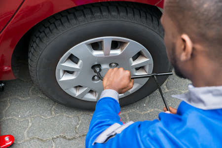 Young African Mechanic Changing Tire Of A Red Car With Wrench