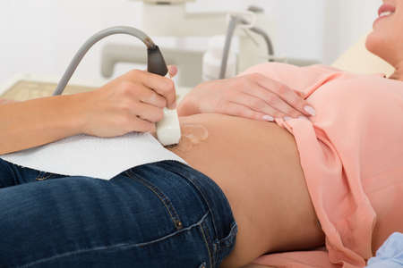 Close-up Of Doctor Moving Ultrasound Probe On Pregnant Woman's Stomach In Hospital