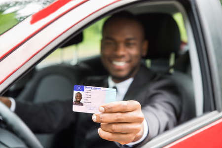 Happy Young African Businessman Showing His Driving License From Open Car Windowの写真素材