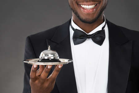 Portrait Of Happy African Waiter Holding Service Bellの写真素材