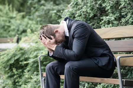 Photo Upset Young Businessman Sitting On Benchの写真素材