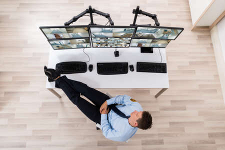High Angle View Of Security Guard Sleeping In Front Of Multiple Computers Showing CCTV Footage