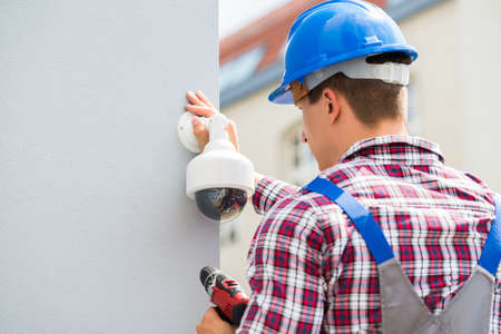 Young Male Technician Installing Camera On Wall Using Electric Cordless Drillの写真素材