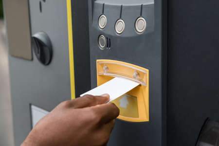 Close-up Of Person's Hand Inserting Ticket Into Parking Machine To Pay For Parking