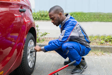 Young African Mechanic Changing Tire Of A Red Car With Wrenchの写真素材