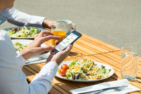Person Chatting On Mobile Phone With Food And Glass Of Juice On Tableの写真素材