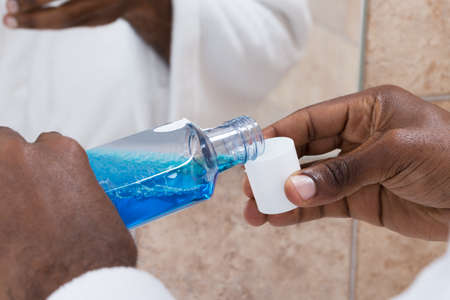 Close-up Of Person Hands Pouring Blue Mouthwash Into Bottle Capの写真素材
