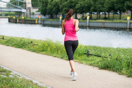Rear View Of Sporty Young Woman Running On Path