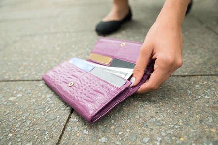 Close-up Of A Woman Picking Up Fallen Wallet On Streetの写真素材