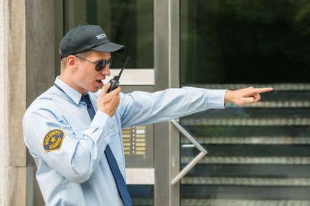 Young Male Security Guard Gesturing While Using Walkie-talkieの写真素材