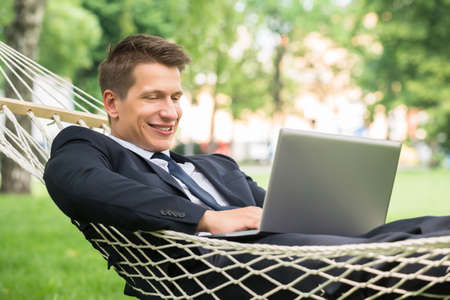Happy Young Man Lying In Hammock Using Laptopの写真素材