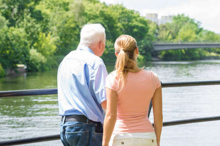 Rear View Of A Young Woman With Her Father Looking At Lake