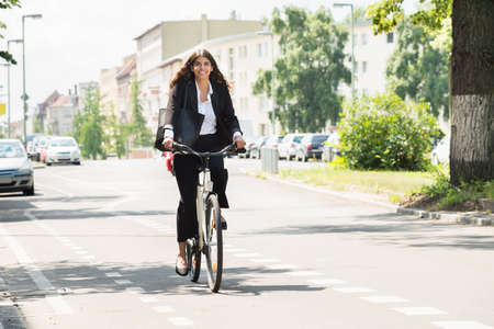 Smiling Young Businesswoman Riding Bicycle On Streetの写真素材