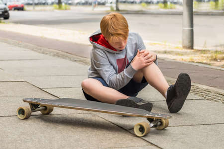 Boy Looking At His Injured Leg Sitting Near Skateboardの写真素材