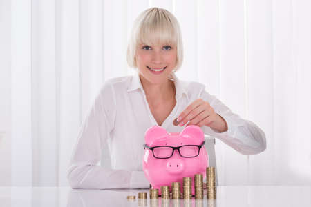 Portrait Of A Happy Young Businesswoman Inserting Coin In Piggybankの写真素材