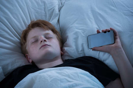 Boy Sleeping On Bed With His Mobile Phoneの写真素材