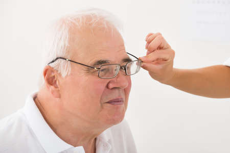 Close-up Of An Optician Helping Senior Male Patient With New Eyeglasses