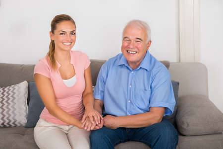 Smiling Young Woman Sitting On Sofa Holding Her Father's Hand At Home