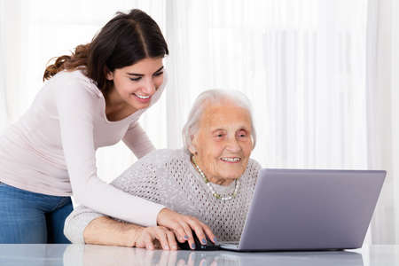 Young Woman Helping Her Grandmother For Using A Laptop On Desk At Homeの写真素材
