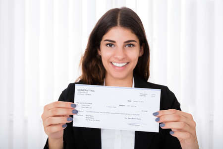 Successful Businesswoman Showing Cheque On Desk In Office