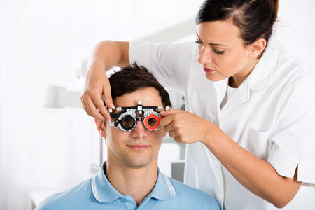 Young Female Optometrist Checking Male Patient's Vision With Trial Frame At Eye Clinic
