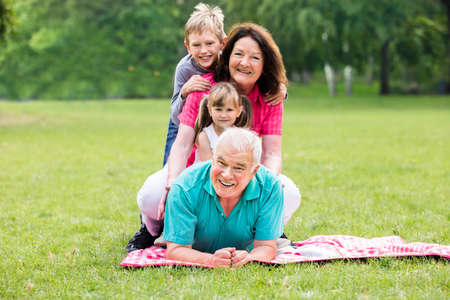 Happy Grandparents And Grandchildren Having Fun Lying On Grass In Parkの写真素材