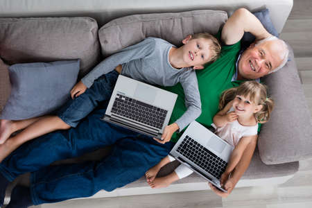 High Angle View Of Grandfather With Kids And Laptop Computers At Homeの写真素材