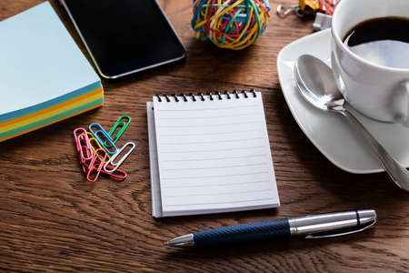 High Angle View Of Notepad With Paper Clips And Coffee Cup On Wooden Desk