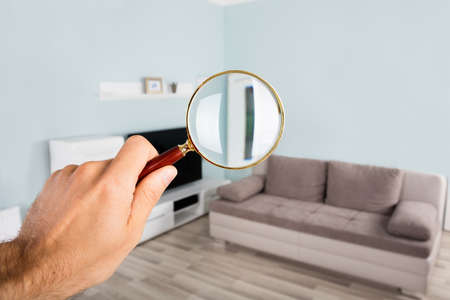 Close-up Of Person Hand Checking Living Room Using Magnifying Glass In Houseの写真素材