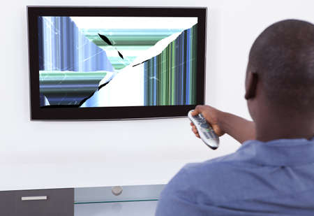 African Man With Remote Control In Front Of Television Showing Distorted Screen