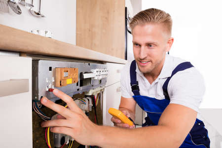 Young Male Technician Fixing Dishwasher With Digital Multimeterの写真素材