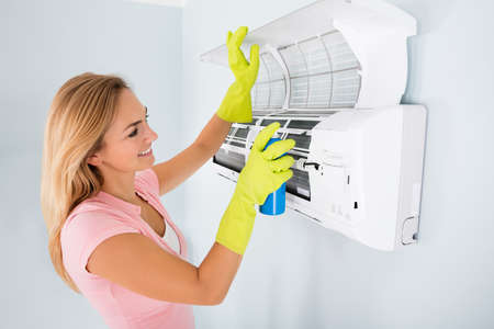 Young Happy Woman Cleaning The Air Conditioner With Spray Bottle At Homeの写真素材