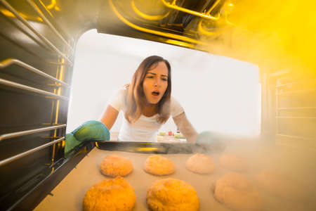 Shocked Young Woman Looking At Burnt Cookies In Ovenの写真素材