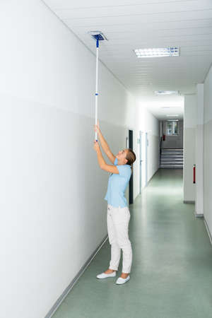Young Woman Cleaning The Ceiling With Mop On The Corridor Of The Buildingの写真素材