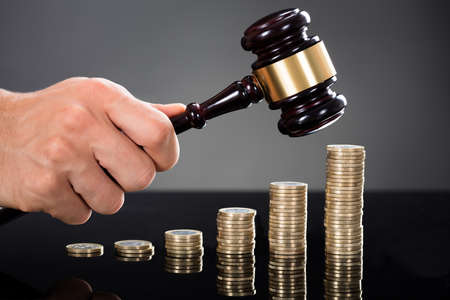 Close-up Of A Judge Hands Hitting Gavel In Front Of Stacked Coins At Deskの写真素材