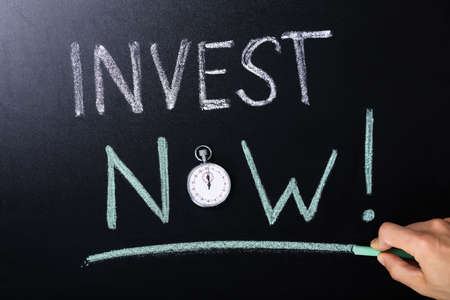 Close-up Of Invest Now Concept With Stopwatch On Blackboardの写真素材