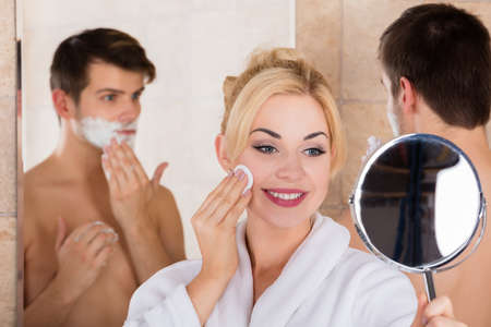 Portrait Of A Man Shaving And Her Wife Cleaning Her Face In Mirror At Bathroomの写真素材