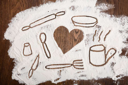 Kitchen Utensil With Heart Shape Drawn On White Flour At Wooden Deskの写真素材